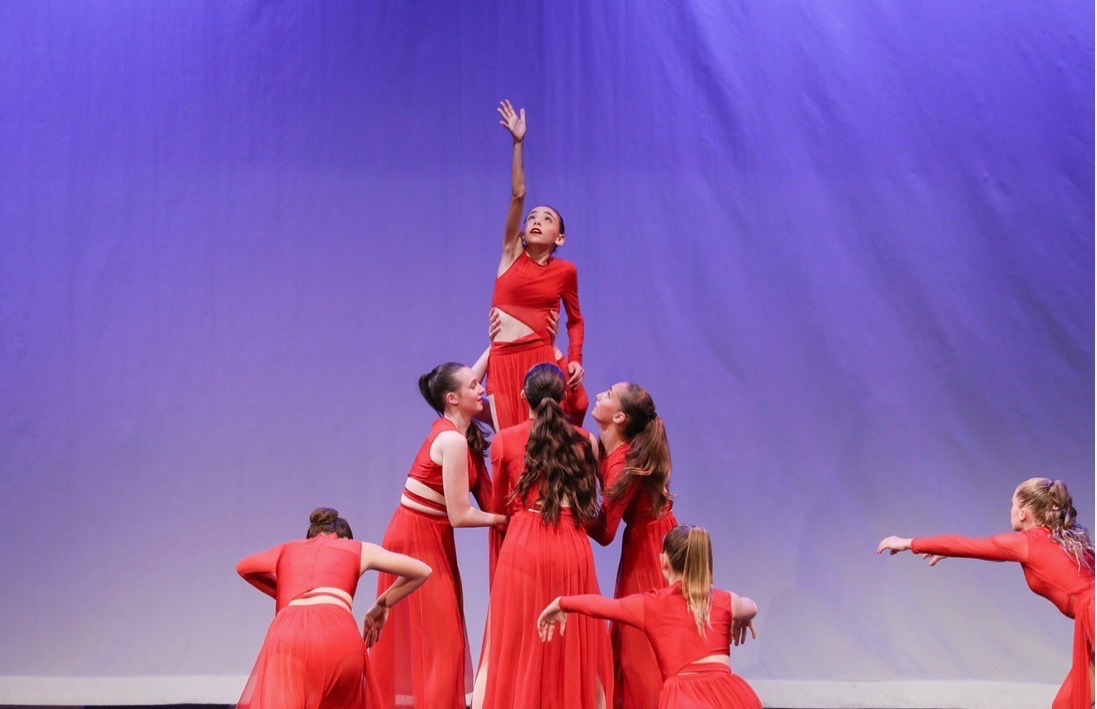Contemporary dancers in red lifting a soloist on stage