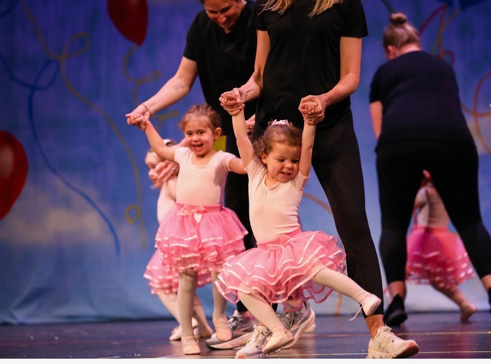Toddlers in pink tutus dancing on stage with their teachers