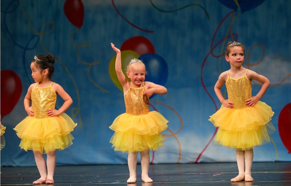 Young ballerinas in yellow tutus and tiaras posing on stage